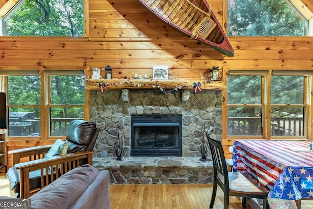 living room with a towering ceiling, hardwood / wood-style flooring, a stone fireplace, and wood walls