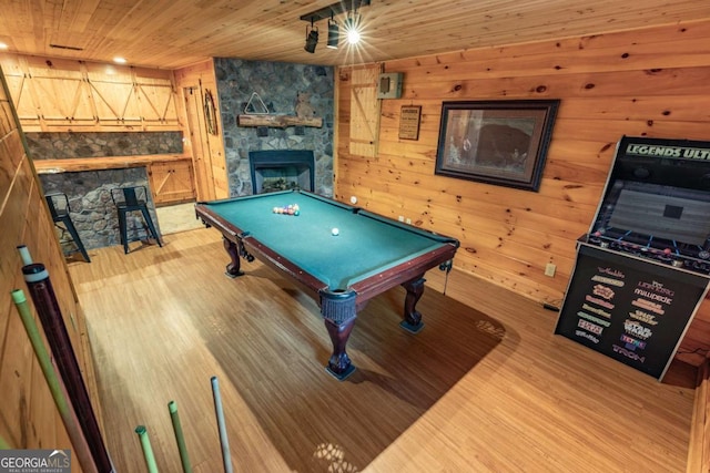 game room with pool table, wooden ceiling, hardwood / wood-style floors, a stone fireplace, and wood walls