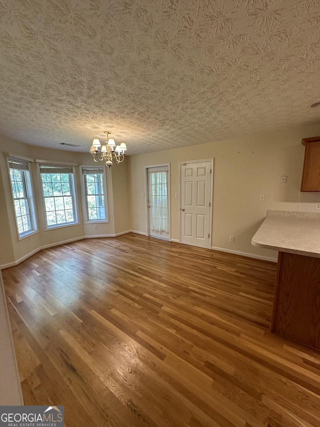 unfurnished dining area with hardwood / wood-style flooring, a textured ceiling, and an inviting chandelier