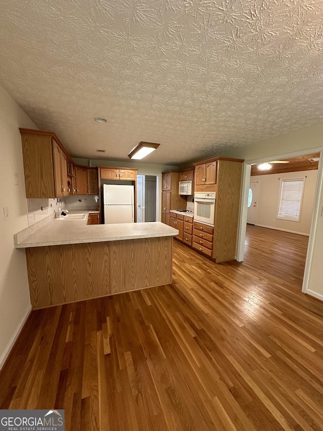 kitchen featuring kitchen peninsula, wood-type flooring, white appliances, and a textured ceiling