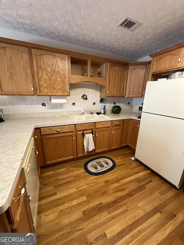 kitchen with sink, backsplash, white fridge, light hardwood / wood-style floors, and a textured ceiling