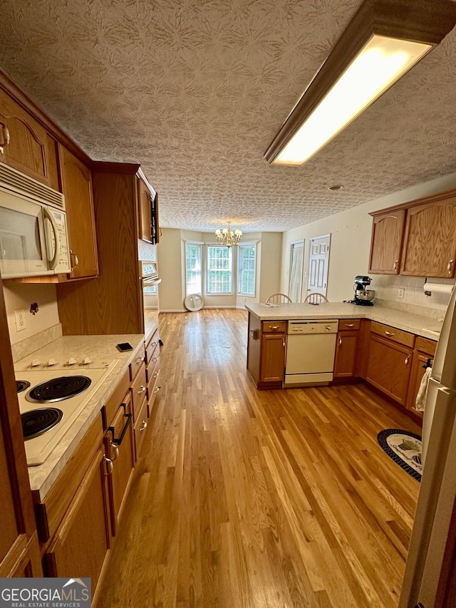 kitchen featuring kitchen peninsula, a textured ceiling, white appliances, an inviting chandelier, and light hardwood / wood-style floors