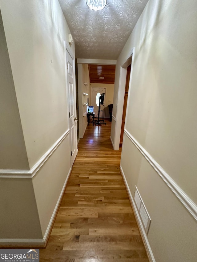 corridor with a textured ceiling and light hardwood / wood-style flooring