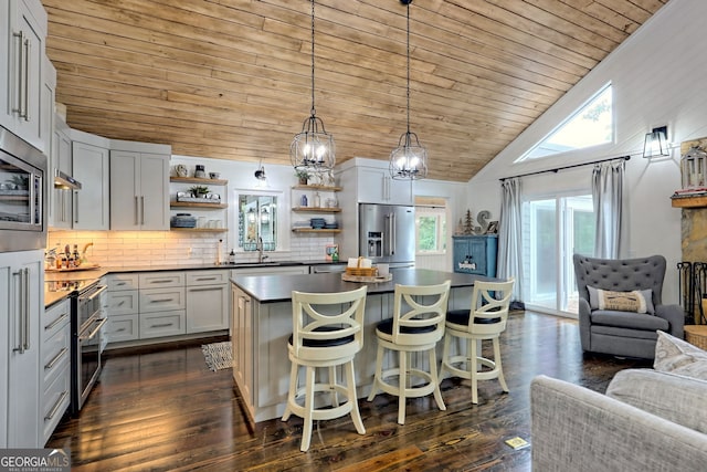 kitchen featuring backsplash, vaulted ceiling, appliances with stainless steel finishes, a kitchen island, and a kitchen bar