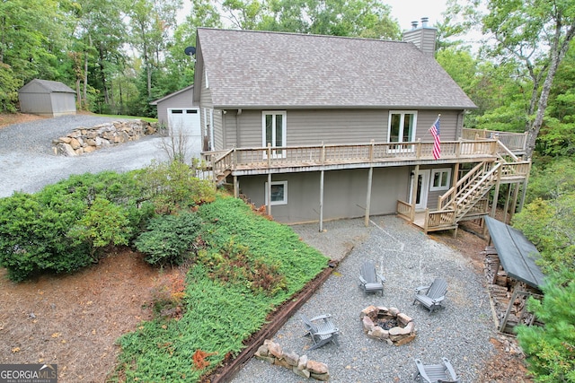 rear view of house with a deck, a storage shed, central AC, a fire pit, and a garage