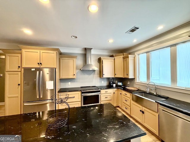 kitchen featuring dark stone counters, wall chimney range hood, sink, light brown cabinetry, and appliances with stainless steel finishes