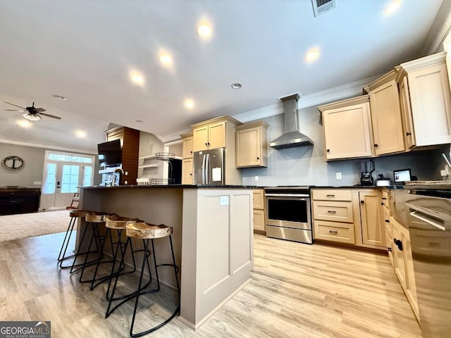 kitchen featuring ceiling fan, a center island, stainless steel appliances, wall chimney range hood, and ornamental molding