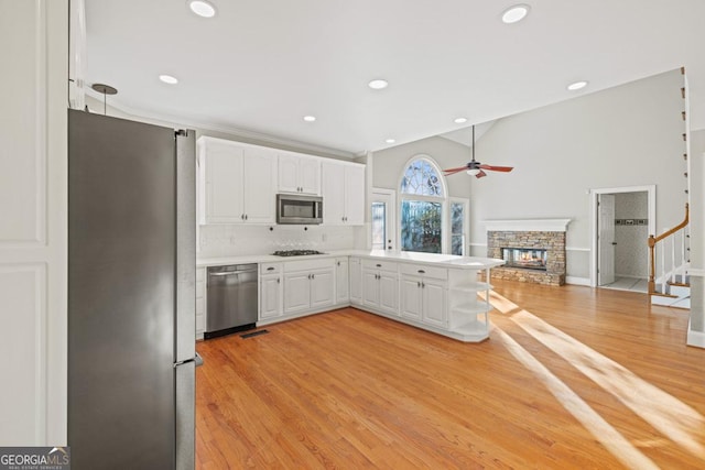 kitchen with white cabinetry, tasteful backsplash, a stone fireplace, light hardwood / wood-style flooring, and appliances with stainless steel finishes