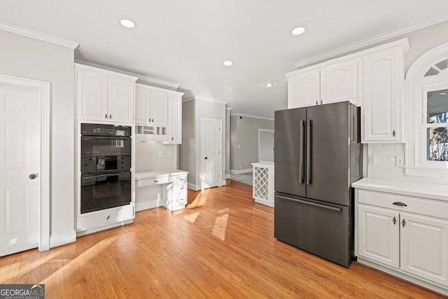 kitchen featuring crown molding, decorative backsplash, double oven, white cabinetry, and stainless steel refrigerator