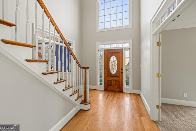 foyer entrance with light hardwood / wood-style flooring, a towering ceiling, and plenty of natural light