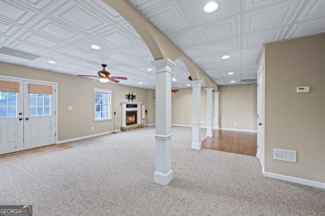 unfurnished living room featuring ceiling fan, french doors, light carpet, and decorative columns