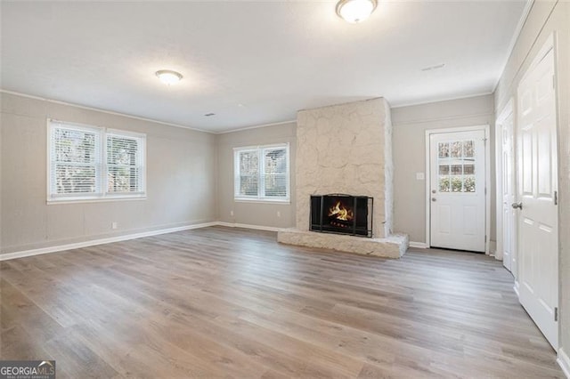 unfurnished living room featuring hardwood / wood-style flooring, a stone fireplace, and ornamental molding