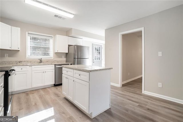 kitchen featuring light stone counters, a center island, white cabinets, and appliances with stainless steel finishes