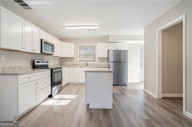 kitchen with light stone counters, stainless steel appliances, a center island, light hardwood / wood-style floors, and white cabinetry