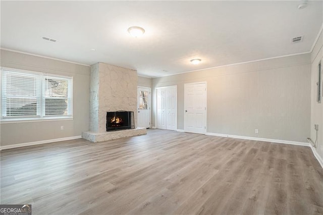 unfurnished living room with a stone fireplace, crown molding, and light hardwood / wood-style flooring