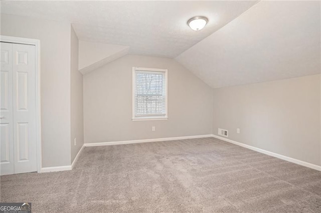 additional living space featuring a textured ceiling, light colored carpet, and lofted ceiling