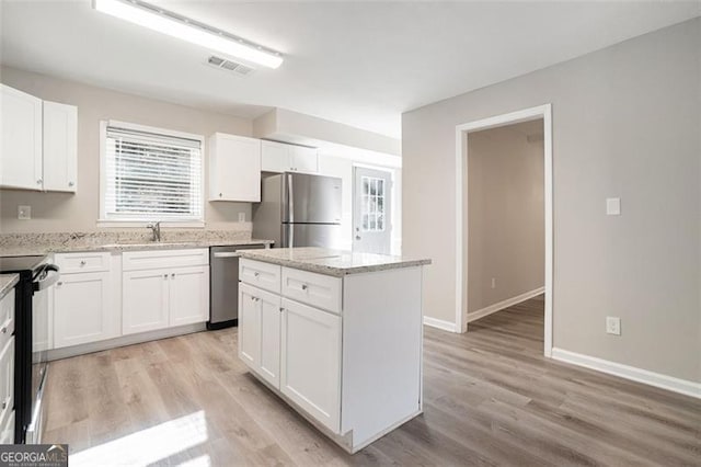 kitchen with white cabinets, sink, a kitchen island, light stone counters, and stainless steel appliances