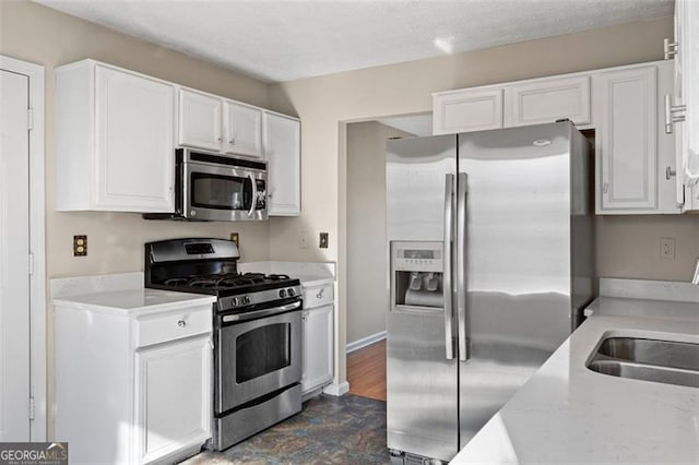 kitchen with light stone counters, stainless steel appliances, white cabinetry, and sink