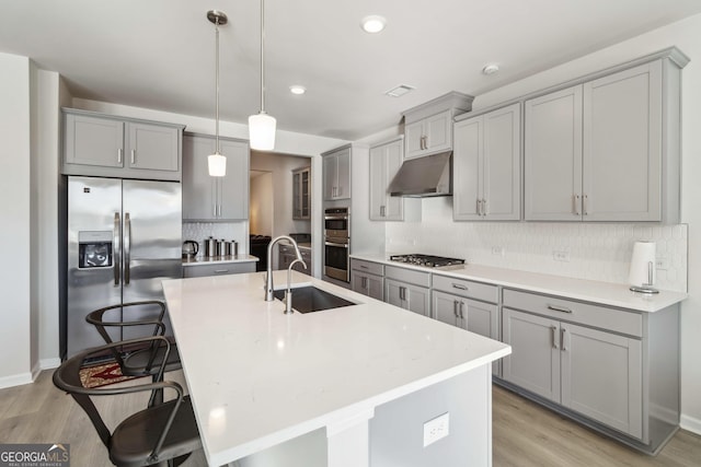 kitchen with appliances with stainless steel finishes, a breakfast bar, sink, pendant lighting, and an island with sink