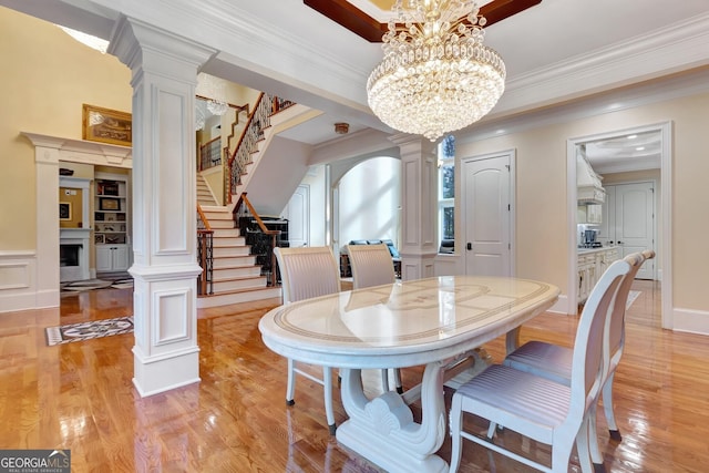 dining space featuring crown molding, light wood-type flooring, an inviting chandelier, and decorative columns