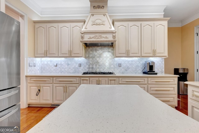 kitchen featuring custom exhaust hood, decorative backsplash, stainless steel refrigerator, crown molding, and gas stovetop