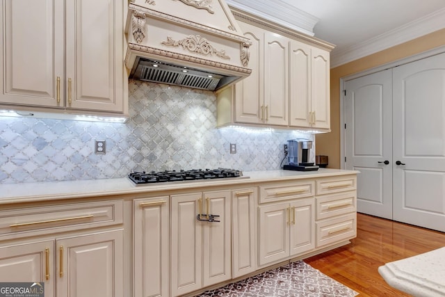 kitchen with backsplash, custom exhaust hood, crown molding, light hardwood / wood-style flooring, and stainless steel gas cooktop