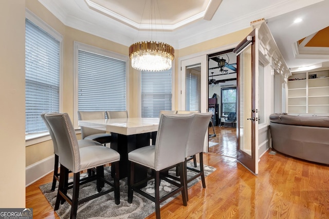 dining space with light hardwood / wood-style floors, a raised ceiling, crown molding, french doors, and a chandelier