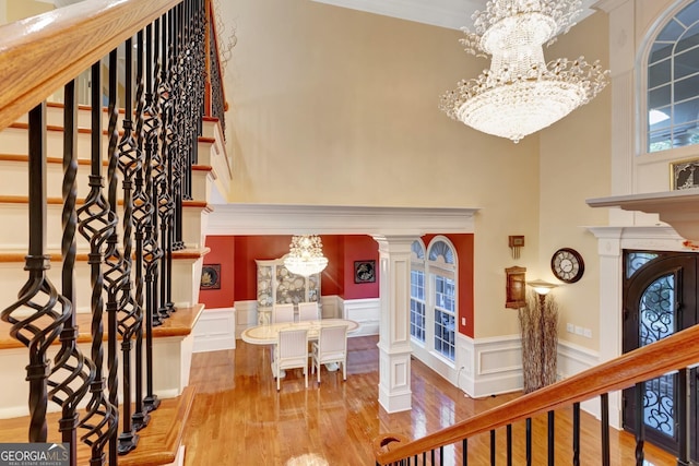 entrance foyer featuring crown molding, light hardwood / wood-style flooring, an inviting chandelier, and decorative columns