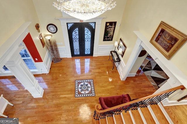 foyer entrance featuring hardwood / wood-style floors, a towering ceiling, french doors, and a notable chandelier