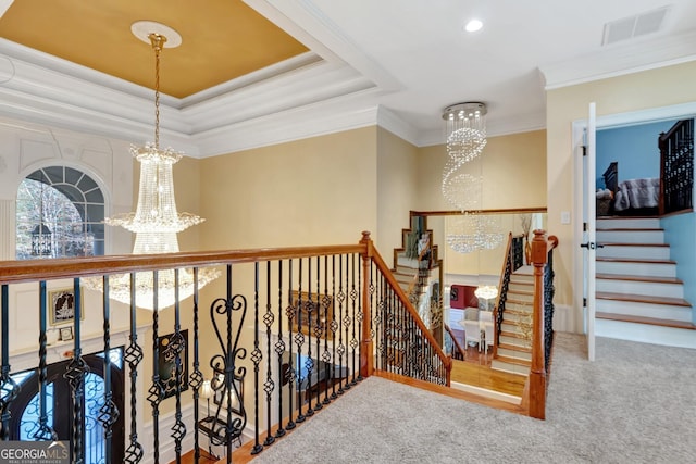 corridor with carpet floors, a tray ceiling, a chandelier, and ornamental molding