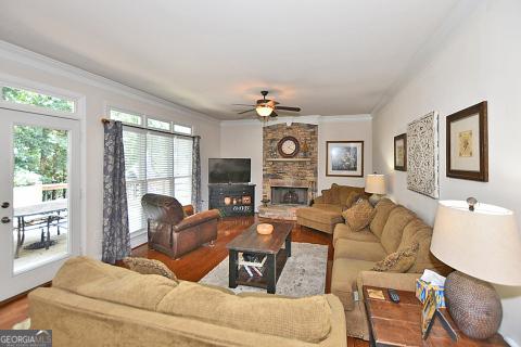 living room featuring hardwood / wood-style floors, ceiling fan, a stone fireplace, and crown molding