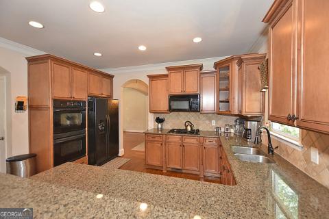 kitchen with light stone countertops, backsplash, crown molding, sink, and black appliances