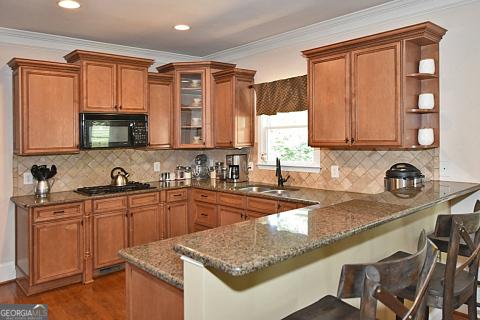 kitchen with kitchen peninsula, a kitchen bar, crown molding, sink, and dark stone countertops