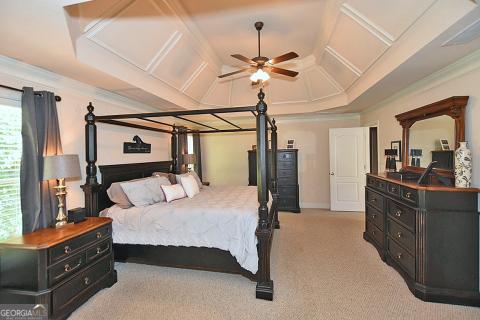 carpeted bedroom with ceiling fan, coffered ceiling, and ornamental molding