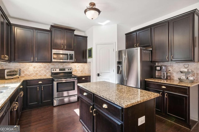 kitchen featuring light stone countertops, tasteful backsplash, dark hardwood / wood-style flooring, a kitchen island, and appliances with stainless steel finishes