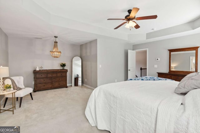 bedroom with light carpet, a tray ceiling, and ceiling fan