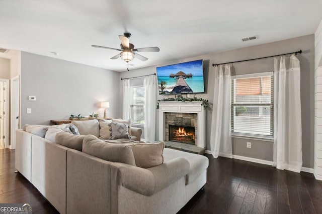 living room featuring a stone fireplace, ceiling fan, and dark hardwood / wood-style flooring