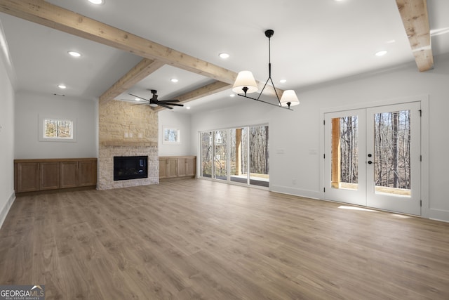 unfurnished living room featuring a stone fireplace, french doors, beam ceiling, and light wood-style floors