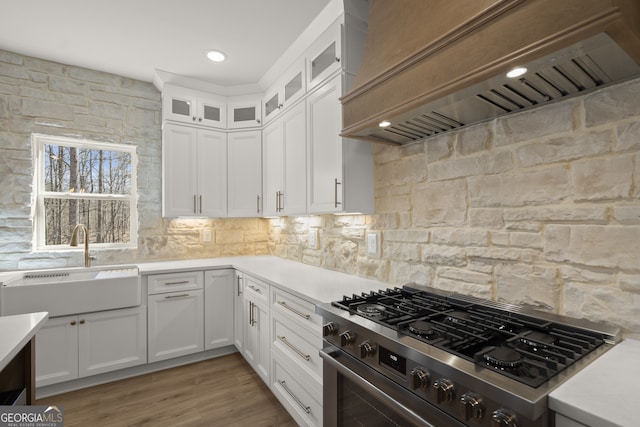 kitchen featuring white cabinets, high end stainless steel range oven, custom range hood, and light countertops