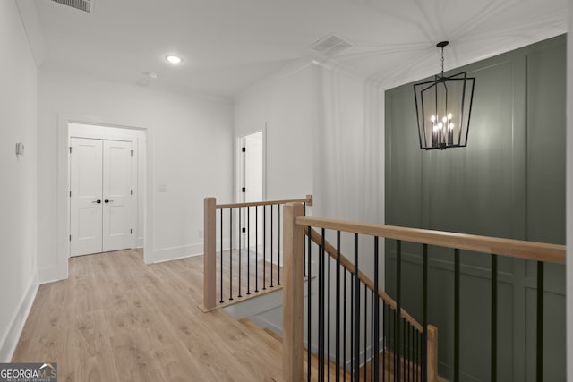 corridor featuring light wood-style flooring, a notable chandelier, an upstairs landing, baseboards, and crown molding