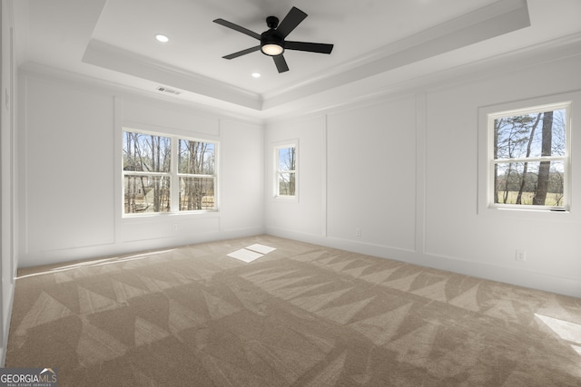 unfurnished room with a tray ceiling, a decorative wall, a wealth of natural light, and light colored carpet