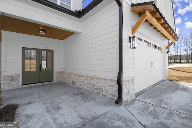 view of exterior entry featuring a garage, french doors, and driveway