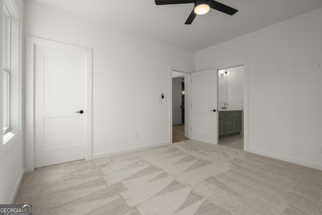 unfurnished bedroom featuring light carpet, baseboards, a ceiling fan, ensuite bath, and a sink