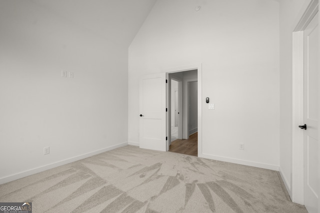 unfurnished bedroom featuring baseboards, high vaulted ceiling, and light colored carpet