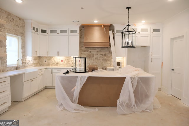 kitchen featuring glass insert cabinets, decorative light fixtures, premium range hood, white cabinetry, and a sink