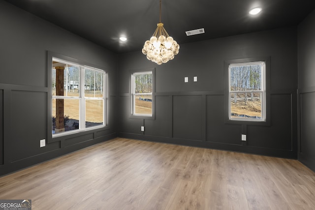 unfurnished dining area with light wood-style floors, a chandelier, visible vents, and a decorative wall