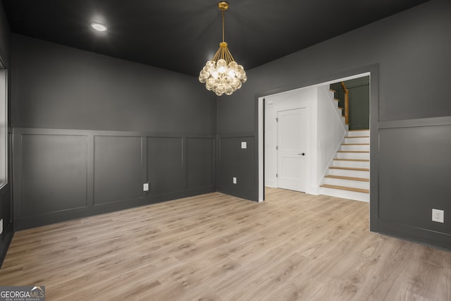 empty room featuring light wood-style floors, stairs, a decorative wall, and a notable chandelier