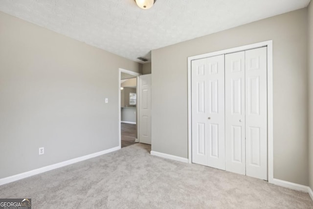 unfurnished bedroom featuring light colored carpet, a textured ceiling, and a closet