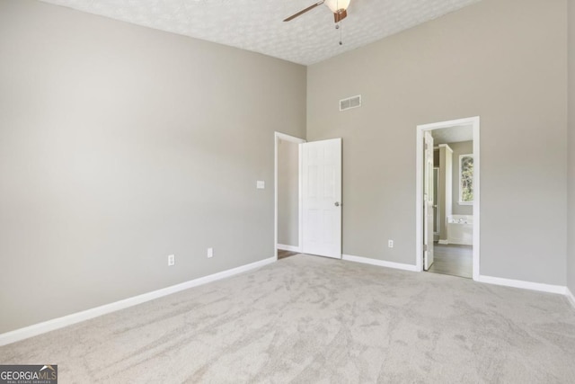 unfurnished bedroom with a textured ceiling, ceiling fan, light carpet, and a high ceiling