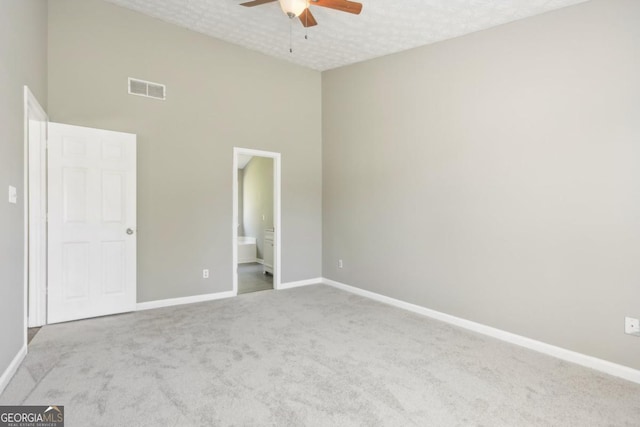 unfurnished bedroom with ceiling fan, a high ceiling, ensuite bathroom, a textured ceiling, and light carpet